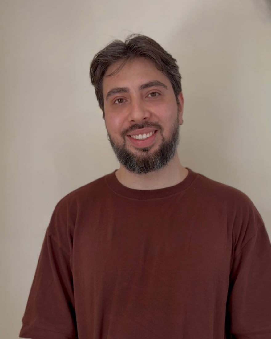 Psicólogo Gustavo Cidade sorrindo, de camiseta marrom, em frente a uma parede clara
